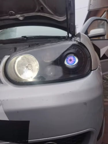 A blue devil eye lit inside a car headlight next to the low beam, hood open - customer photo